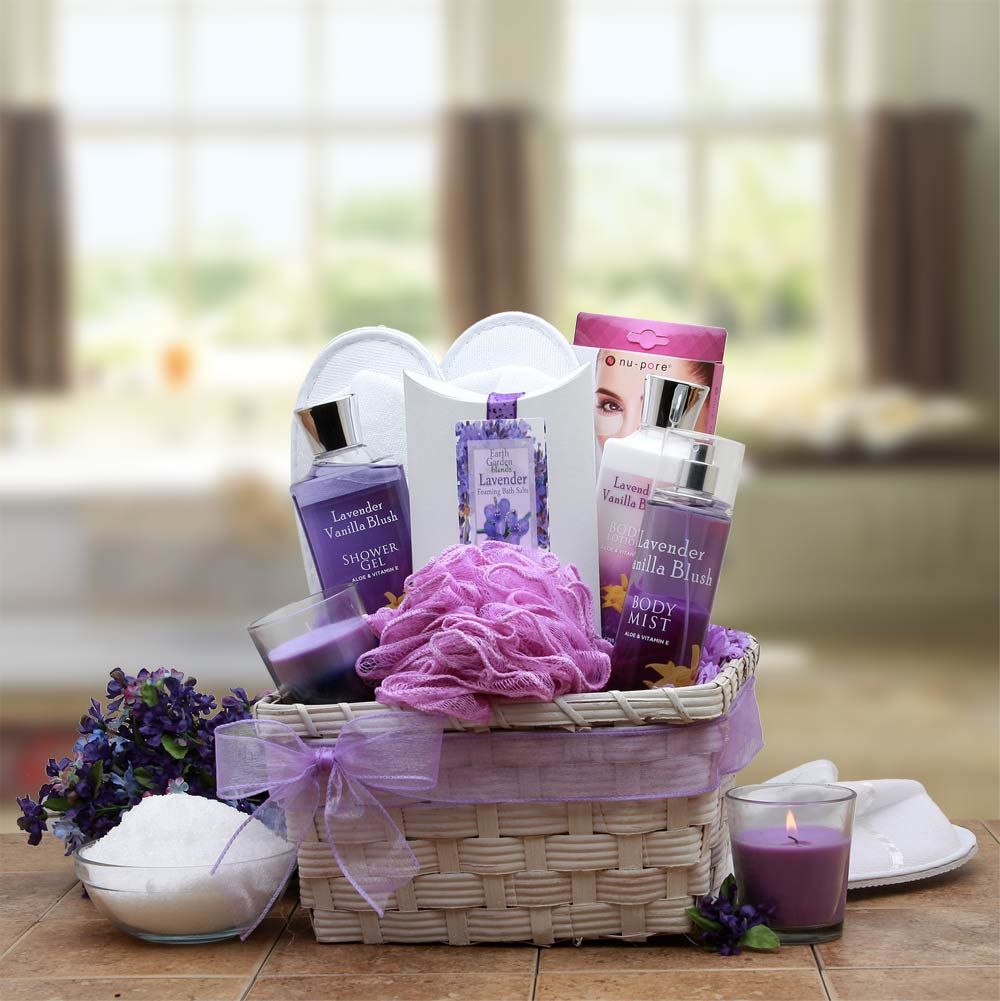 Lavender spa gift basket with bath and body products in a white wicker tray, including lotion, bath gel, body spray, bath salts, loofah, candle, slippers, and eye pads.